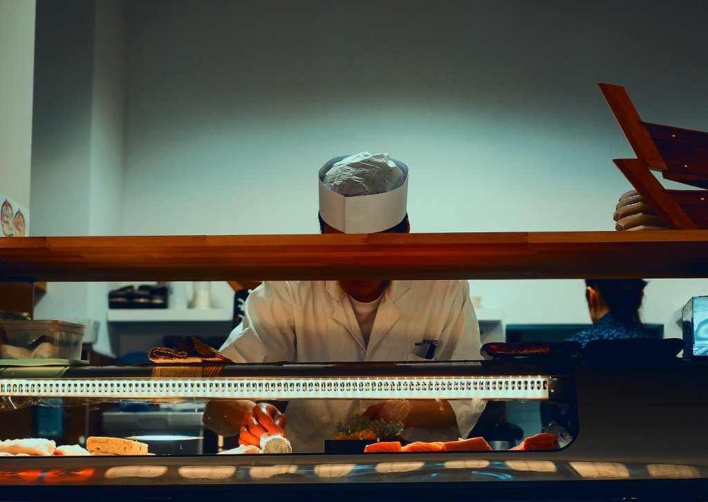 Ein Koch steht hinter der Theke einer Sushi-Bar und bereitet frisches Sushi zu.