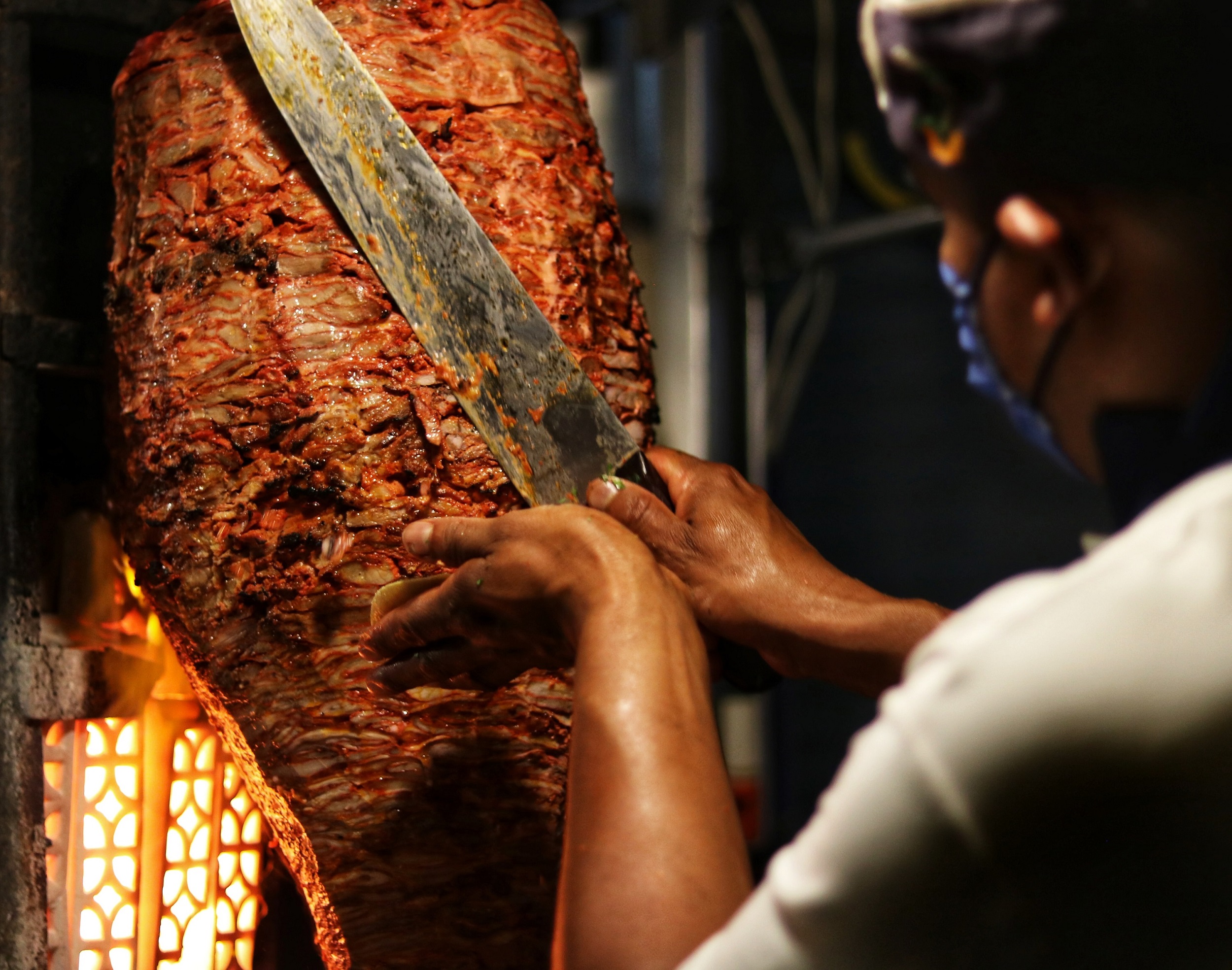 Ein Koch schneidet mit einem Dönermesser das Fleisch in seiner Gastronomie.