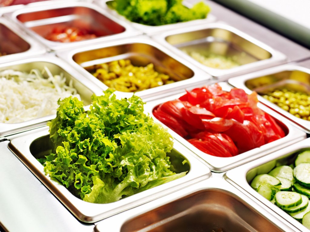 Ein Salatbuffet in einer Gastronomie. Verschiedene Zutaten befinden sich in Metallschüsseln.