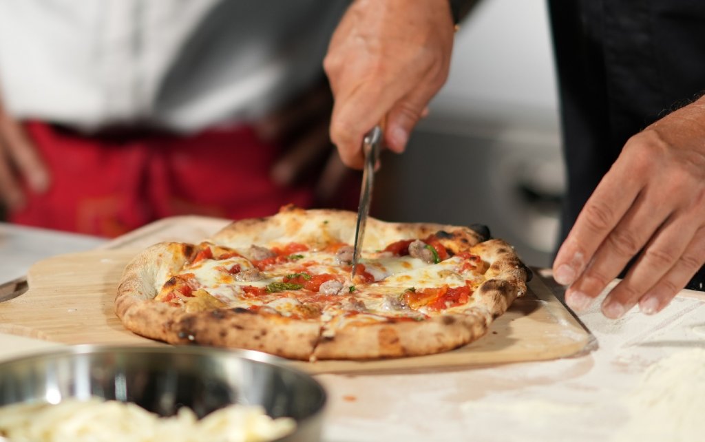 Sternekoch Frank Rosin schneidet in der Küche eine frische neapolitanische Pizza, die er zusammen mit Martino Cesario zubereitet hat.
