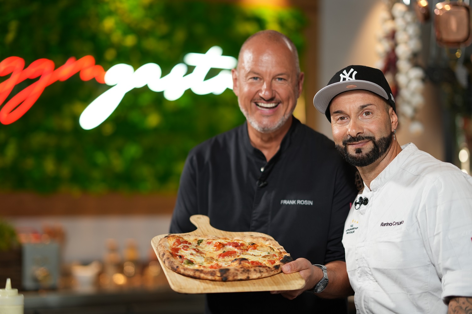 Frank Rosin und Martino Cesario stehen in der Küche von GGM Gastro. Frank Rosin hält eine neapolitanische Pizza, die er zusammen mit Martino Cesario zubereitet hat.
