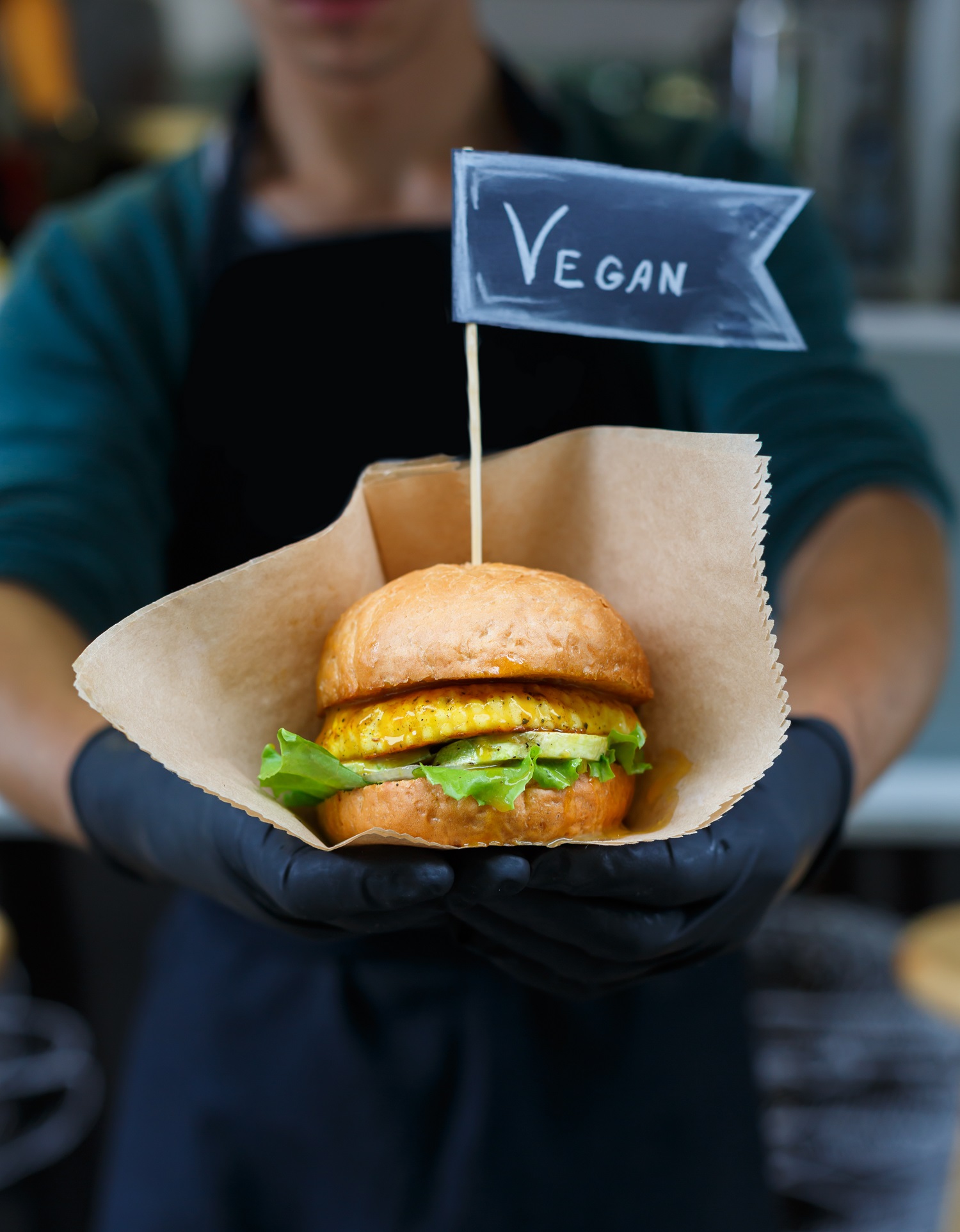 Ein Mitarbeiter in einem Restaurant hält einen veganen Burger. Auf dem Burgerspieß steht "vegan". Das Bild steht symbolisch für personalisierte Ernährung, da Gäste sich in Restaurants Gerichte passend zu ihren individuellen Vorlieben wünschen.