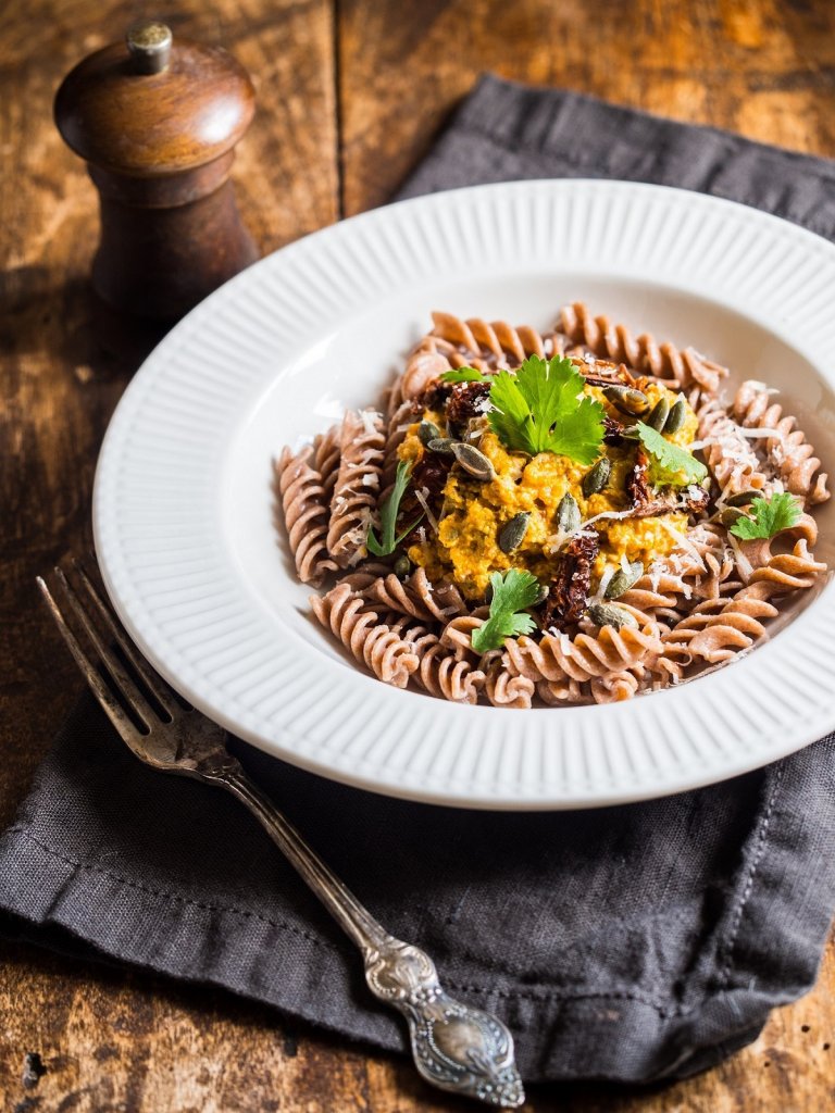 In einem Restaurant steht ein Teller mit Pasta auf einem hölzernen Tisch. Daneben befinden sich eine Gabel und ein Gewürzstreuer. Das Angebot dieser glutenfreien Pasta-Alternative steht symbolisch für personalisierte Ernährung.