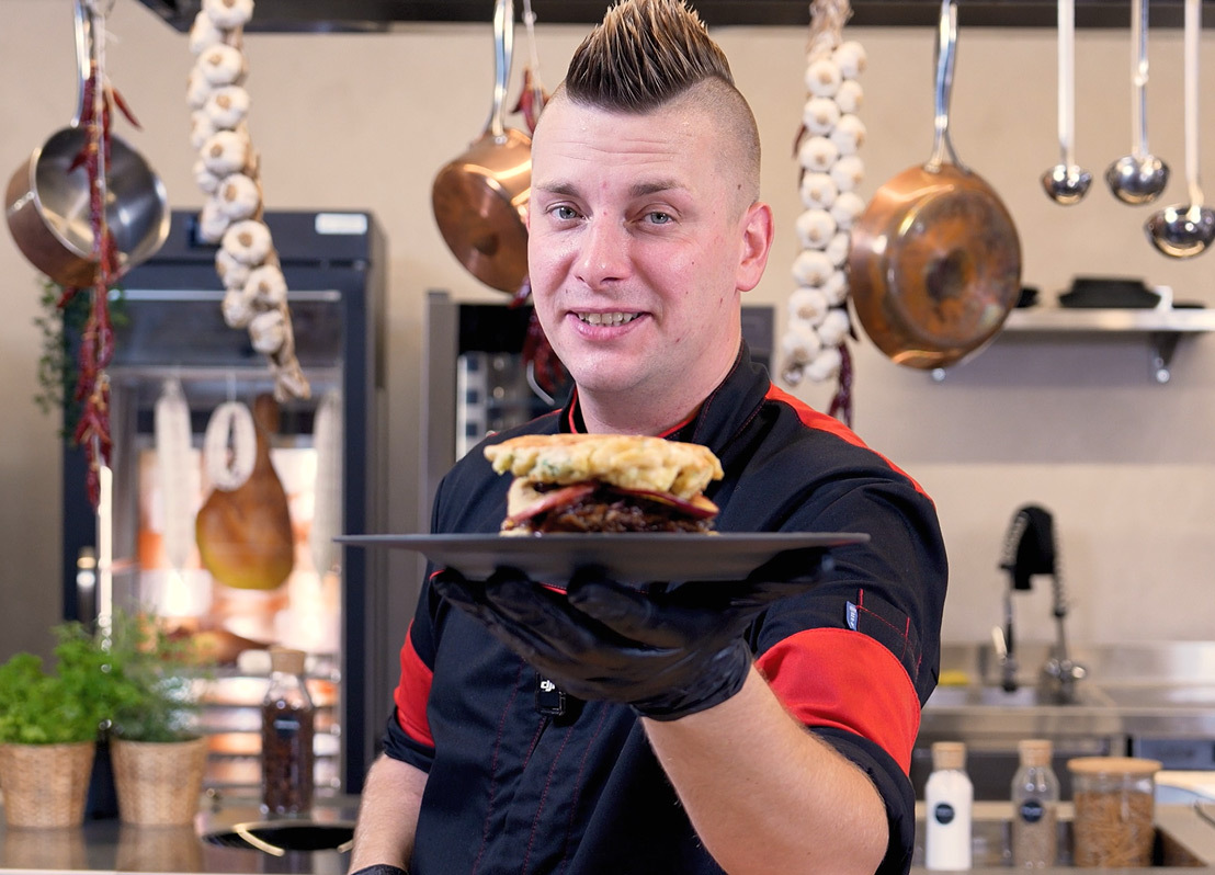 GGM-Koch Harry steht in der Küche und hält einen Teller mit einem Rouladenburger. Damit zeigt er, wie man Fertiggerichte aufpeppen und zu einem außergewöhnlichen Genuss machen kann!