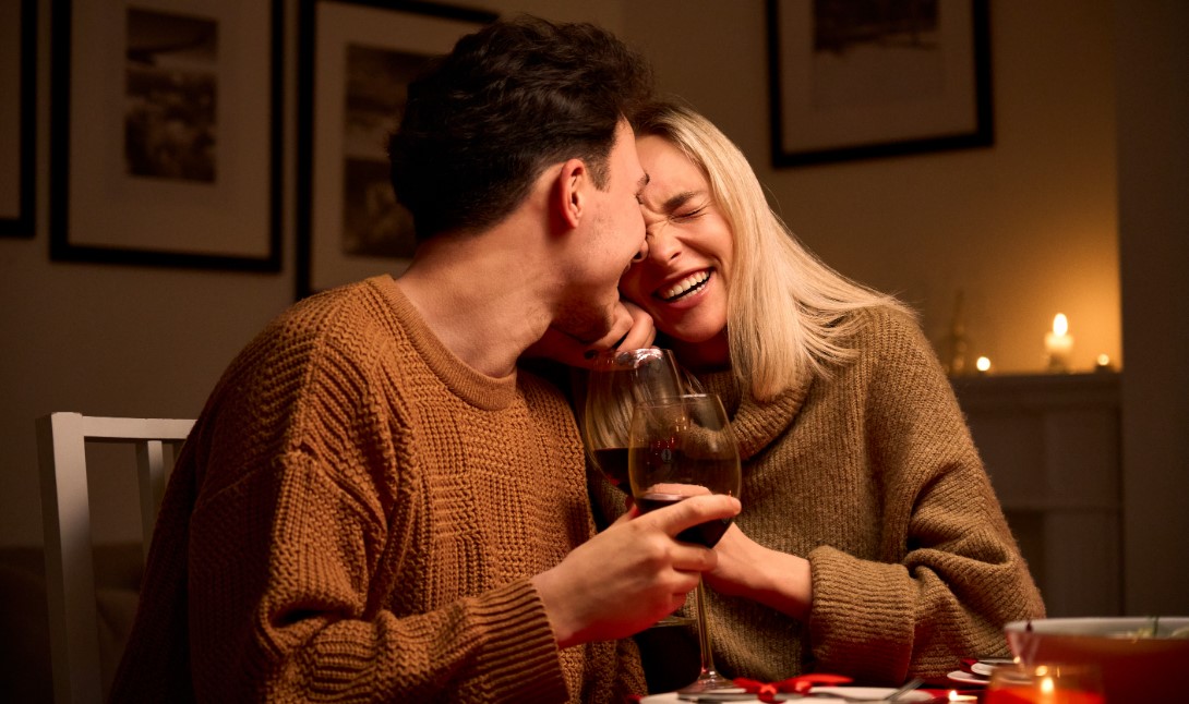 Man sihet ein Pärchen zusammen lachen und mit einem Glas Wein anstoßen.