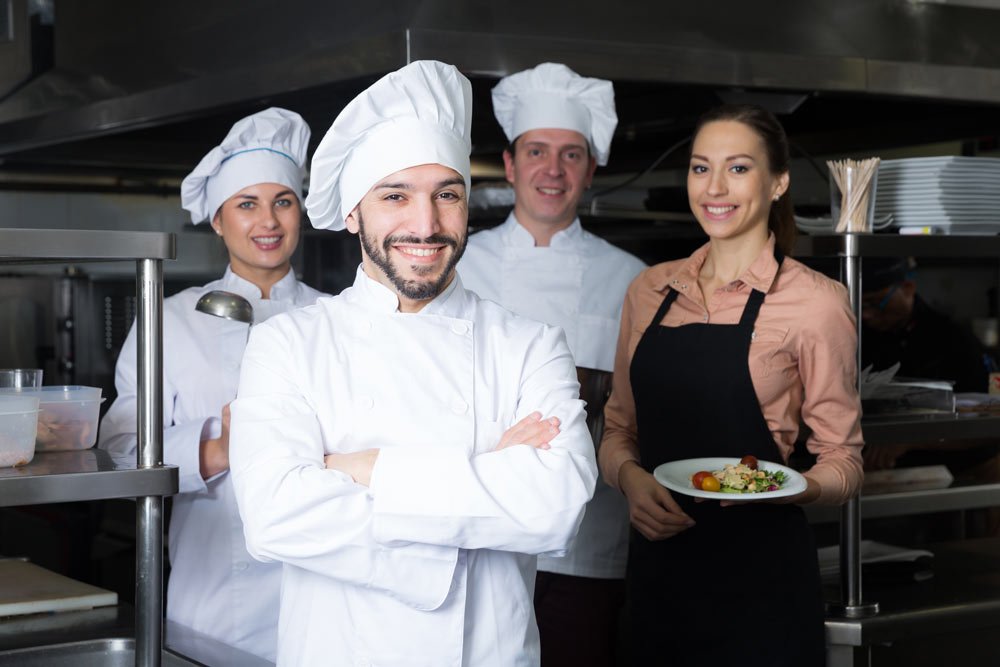 Vier Mitarbeitende stehen lächelnd in der Küche einer Gastronomie.